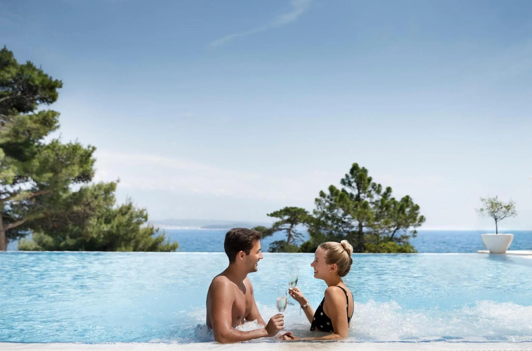 Un couple se fait face dans une piscine à débordement avec vue sur la mer.