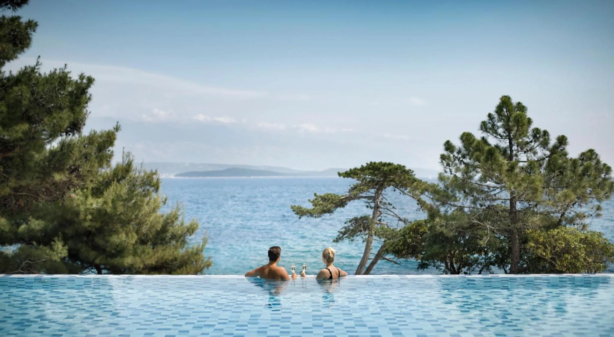 Deux personnes se détendent au bord d'une piscine à débordement avec vue sur la mer.