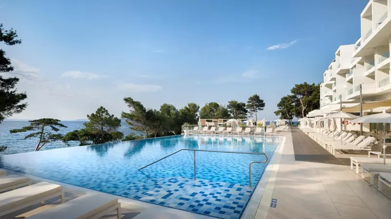 Une piscine à débordement surplombe la mer et une plage de transats.