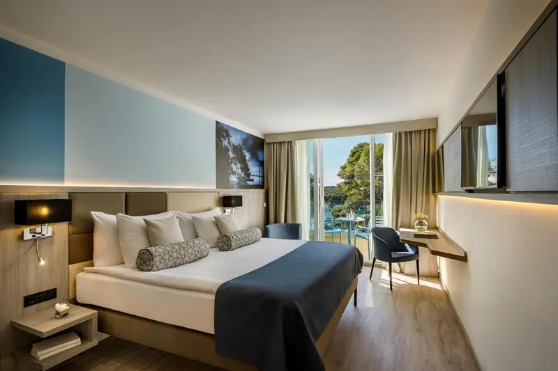 Chambre lumineuse avec un grand lit et une vue sur la végétation.