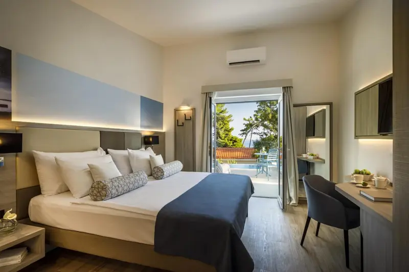 Une chambre lumineuse avec un grand lit et un bureau donnant sur une terrasse.