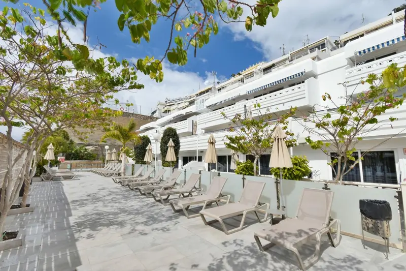 Transats alignés devant un bâtiment blanc avec des balcons et des parasols.