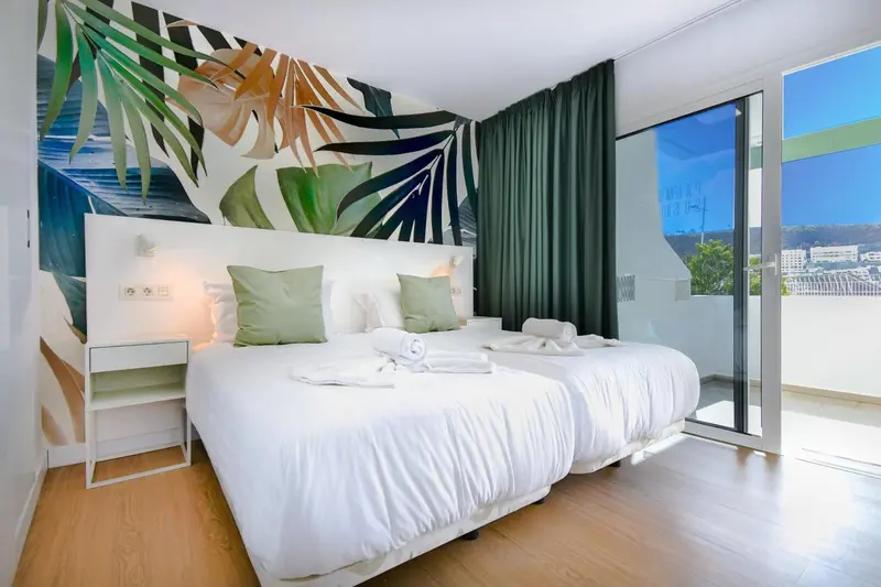 Une chambre lumineuse avec un grand lit et un mur décoré de motifs végétaux.