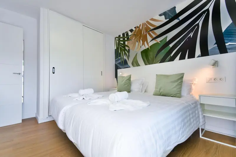 Une chambre lumineuse avec un lit double et une décoration murale tropicale.