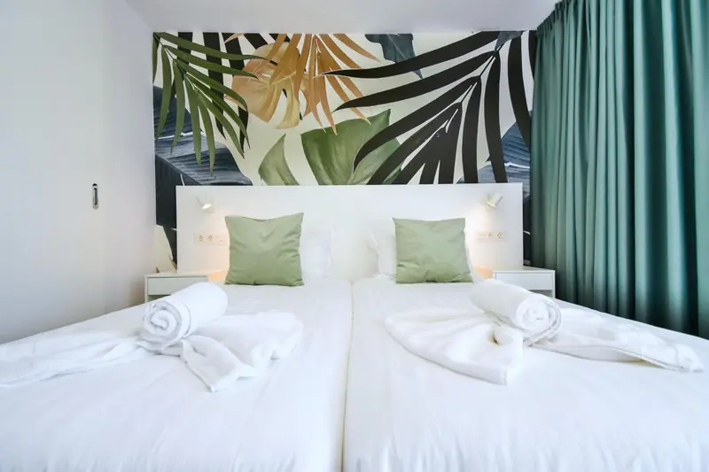 Une chambre lumineuse avec deux lits simples et une décoration tropicale au mur.