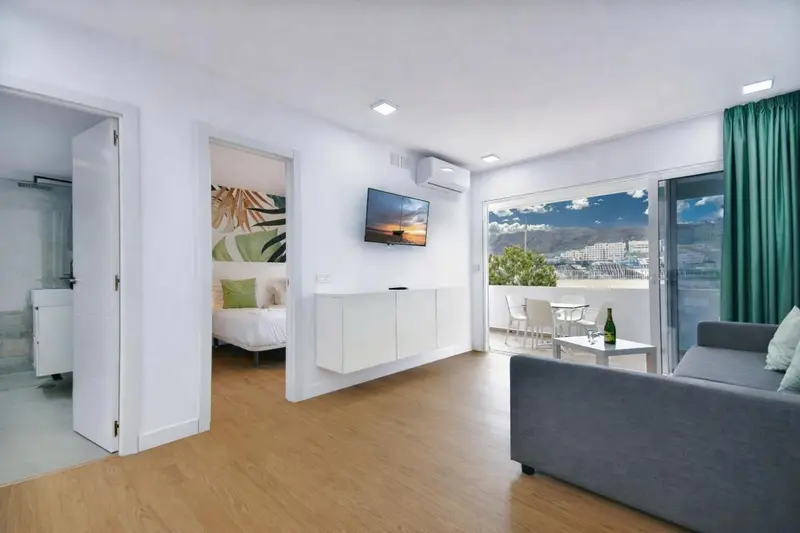 Espace de vie lumineux avec canapé, télévision et accès à une terrasse.