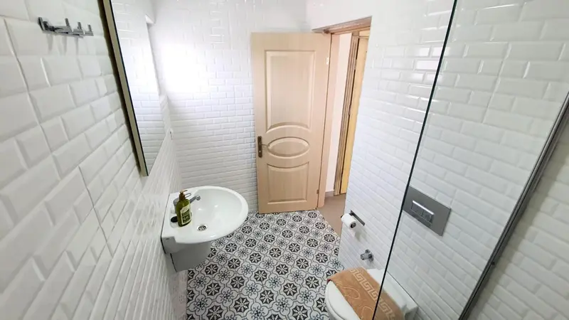 Une salle de bain claire avec carrelage blanc et sol à motifs.