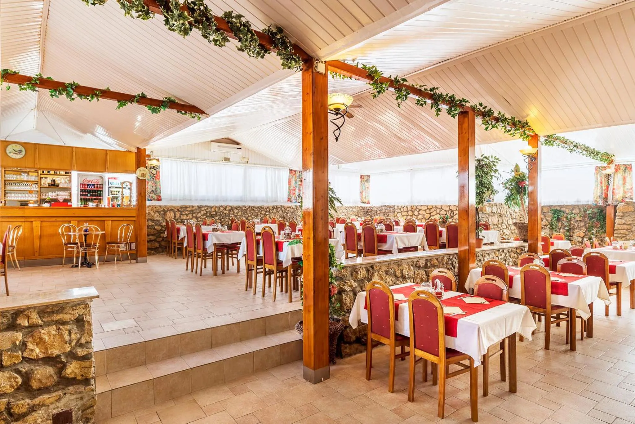 Une salle de restaurant lumineuse avec des tables dressées et un comptoir de boissons.