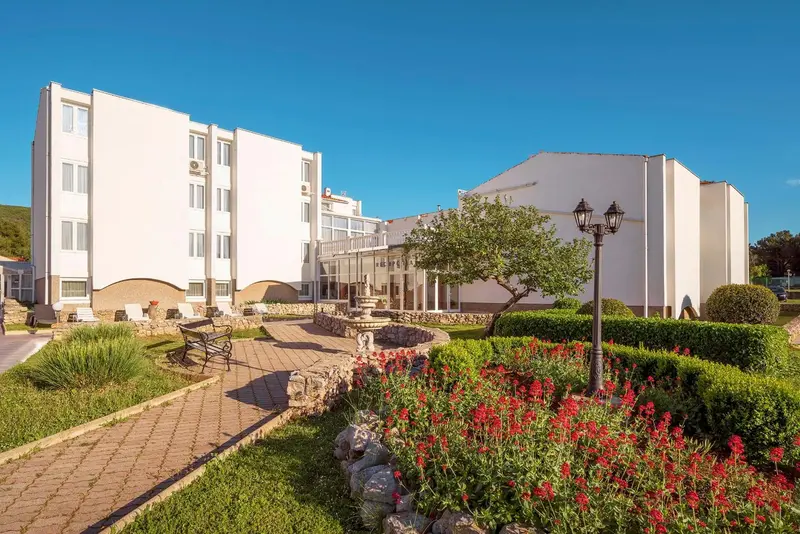 Bâtiment blanc à plusieurs étages avec un jardin fleuri en contrebas.