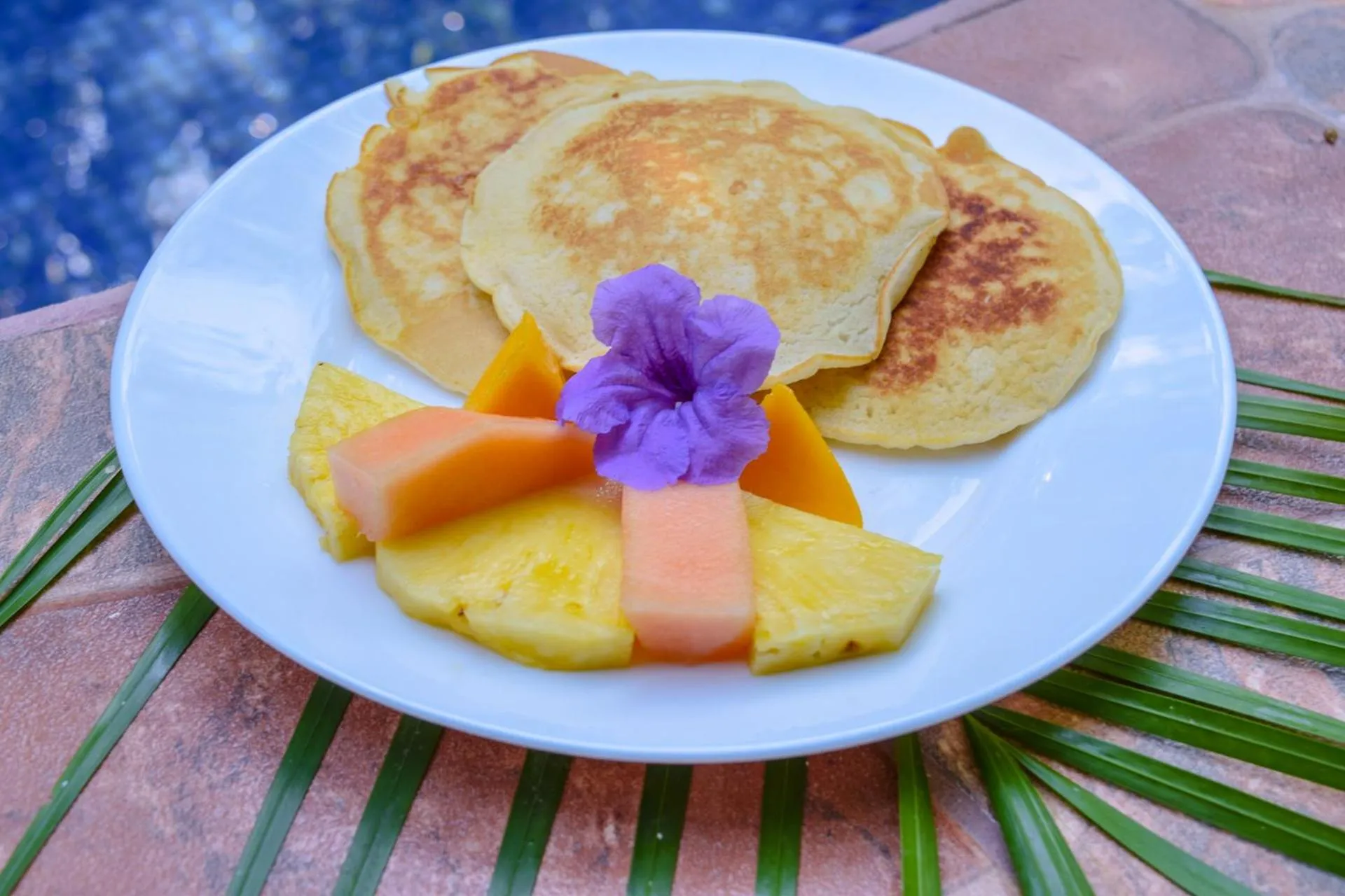 Assiette de crêpes, de fruits frais et d'une fleur violette.