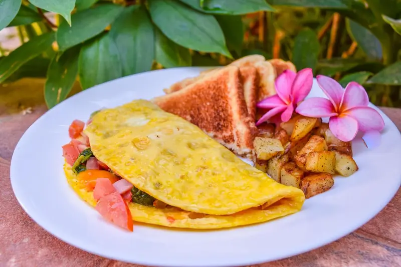 Une assiette avec une omelette, des pommes de terre rissolées et des tranches de pain grillé, décorée d'une fleur.