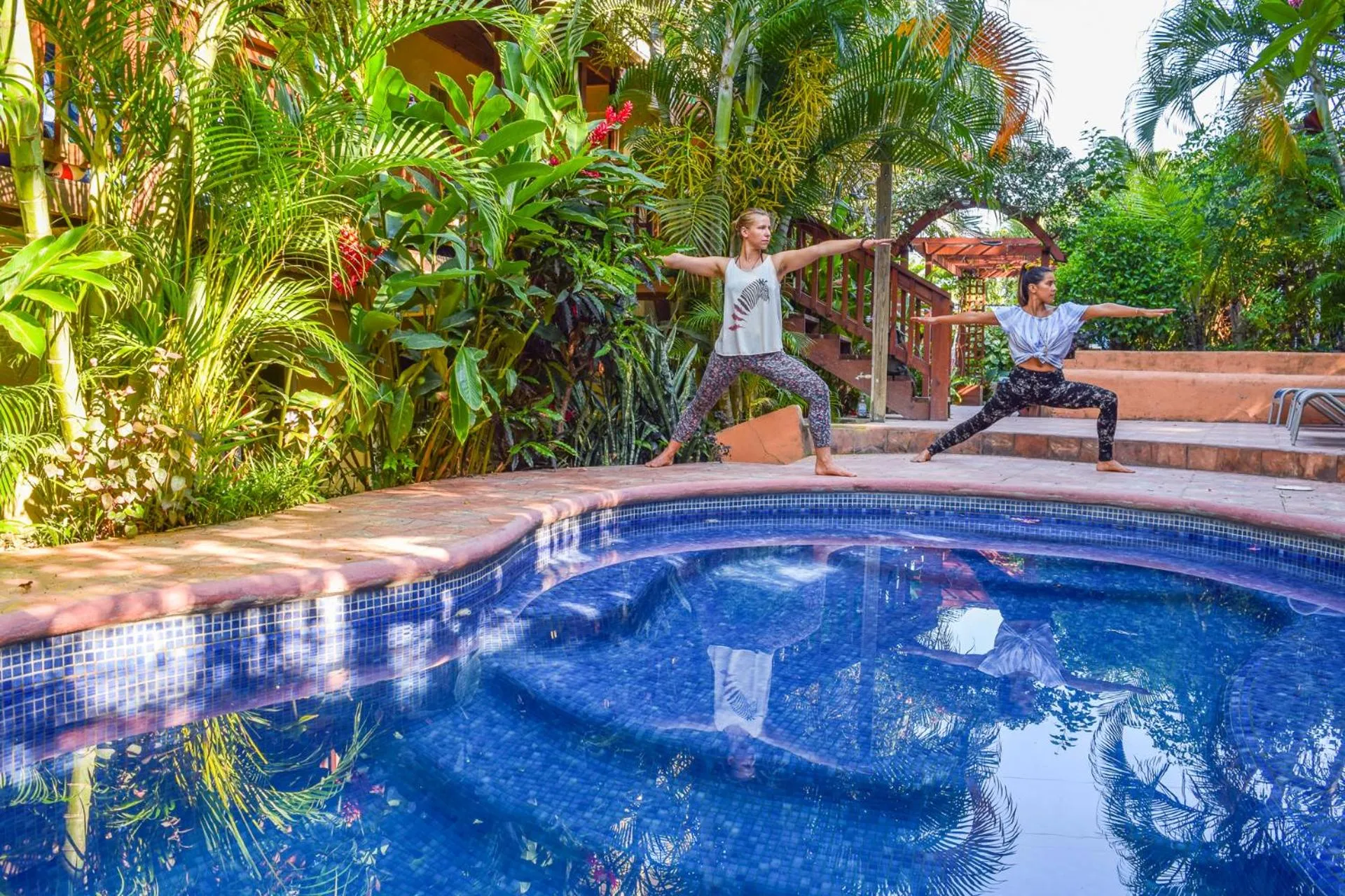 Deux femmes pratiquent le yoga sur une terrasse ensoleillée près d'une piscine.