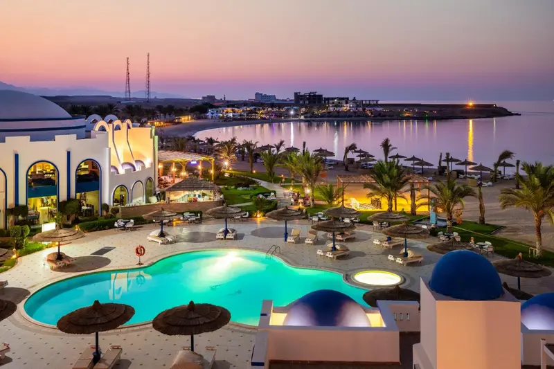 Vue aérienne d'un complexe hôtelier avec piscine et plage au coucher du soleil.