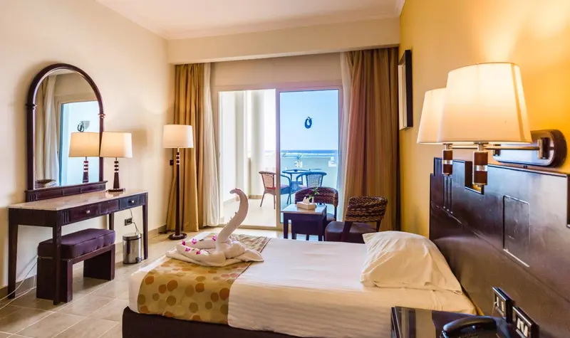 Chambre d'hôtel avec un lit décoré de serviettes en forme de cygne et un balcon.