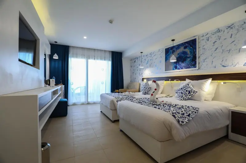 Chambre lumineuse avec deux lits et vue sur l'extérieur.