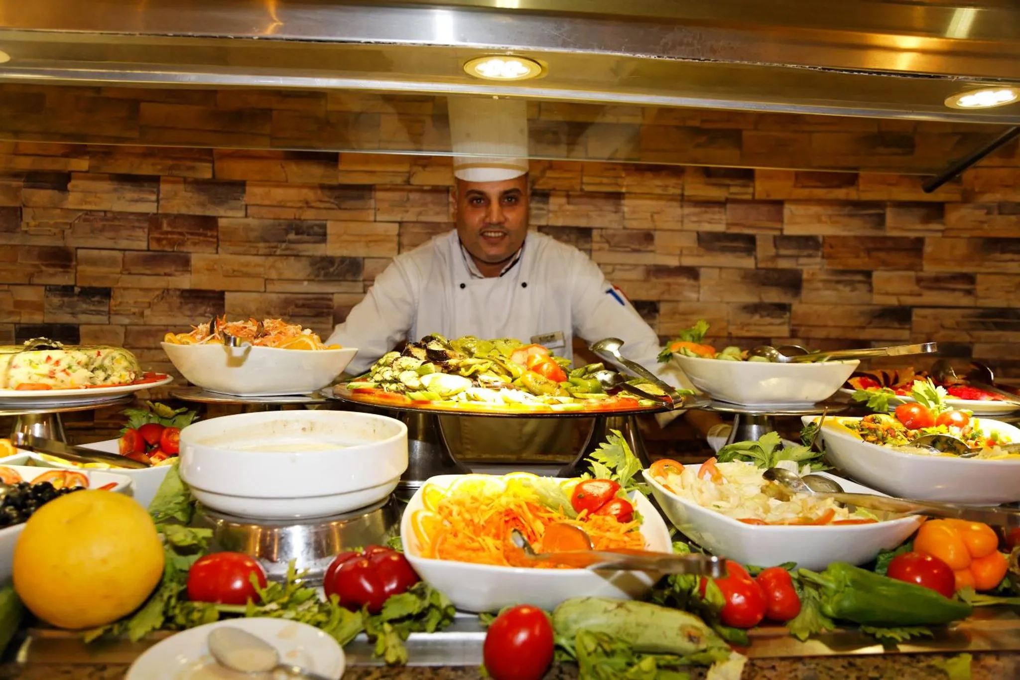 Un chef présente un buffet de salades colorées et variées.