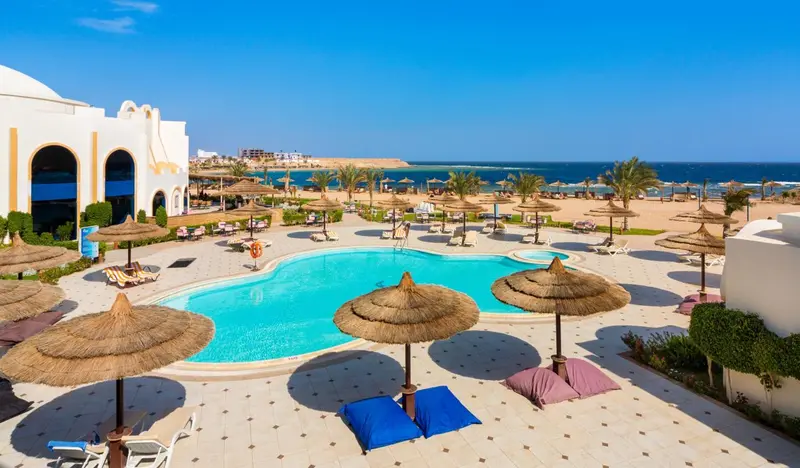 Vue aérienne d'une piscine entourée de transats et de parasols en bord de mer.