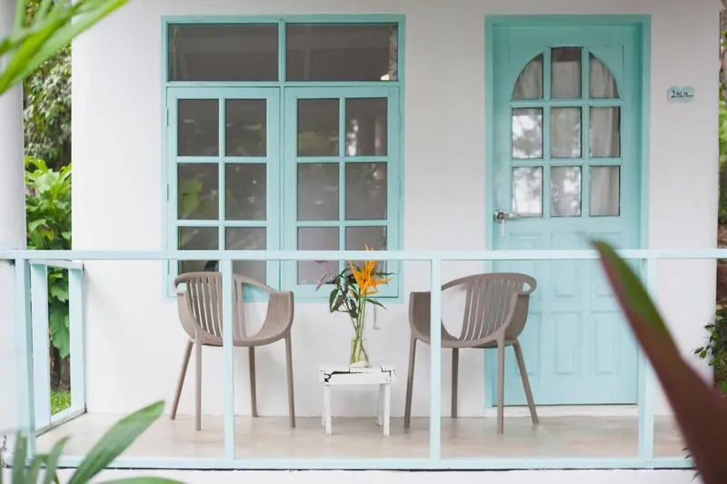 Terrasse avec deux fauteuils et une table ornée de fleurs devant une porte turquoise.