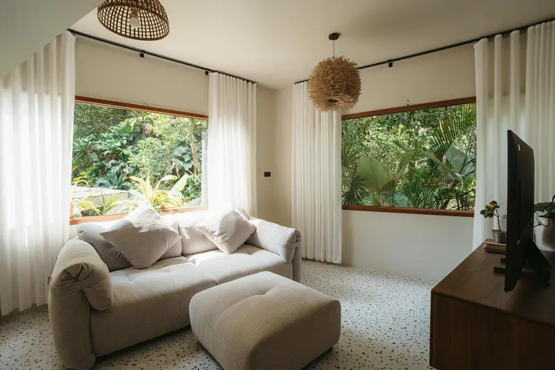 Un canapé confortable est placé devant de grandes fenêtres donnant sur une végétation luxuriante.