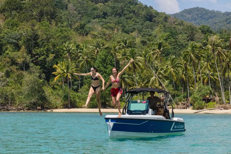Deux femmes sautent d'un bateau amarré dans une baie tropicale.