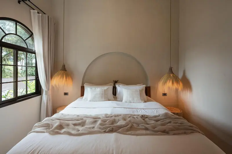 Une chambre lumineuse avec un grand lit recouvert d'une couverture claire et de deux lampes suspendues.