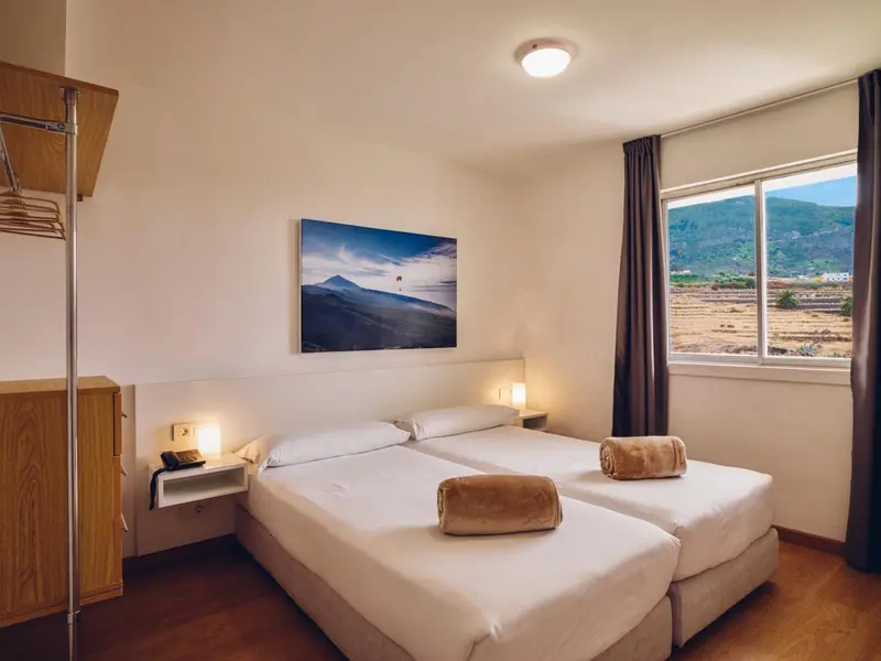Chambre lumineuse avec deux lits simples et une vue sur les montagnes.