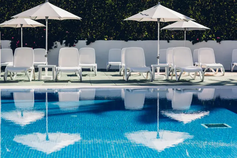 Transats blancs alignés au bord d'une piscine turquoise sous des parasols.