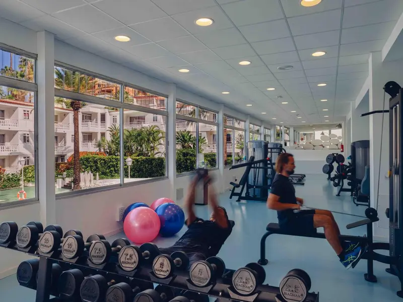 Une salle de sport lumineuse avec des équipements de musculation et une vue sur un paysage tropical.