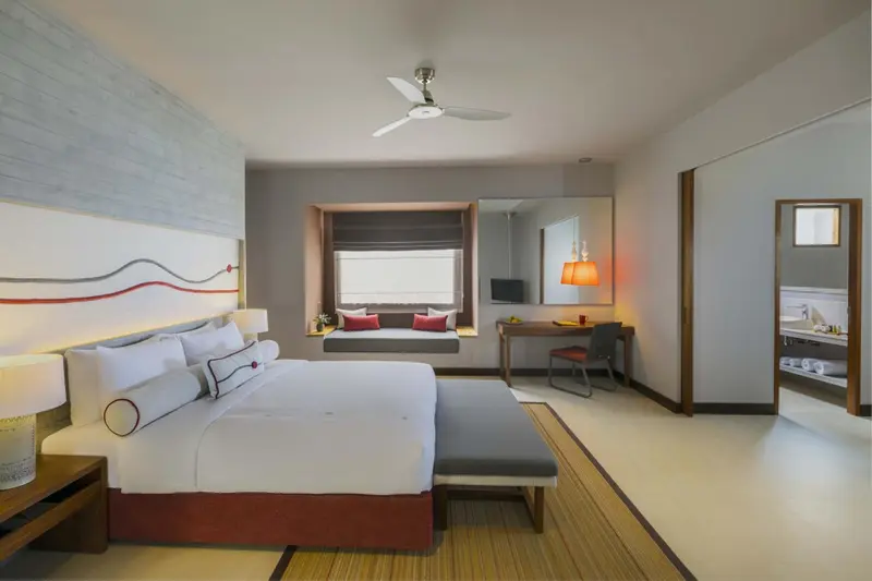 Une chambre lumineuse avec un grand lit et un bureau près de la fenêtre.