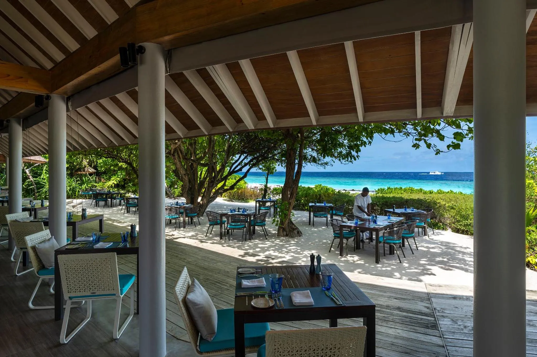 Une salle à manger extérieure avec des tables dressées face à une plage.