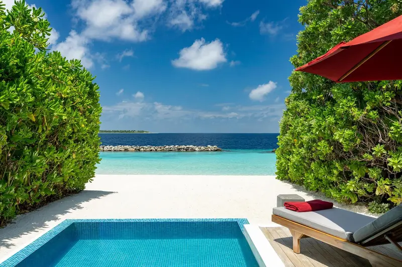 Vue sur une plage de sable blanc et une mer turquoise depuis une terrasse.