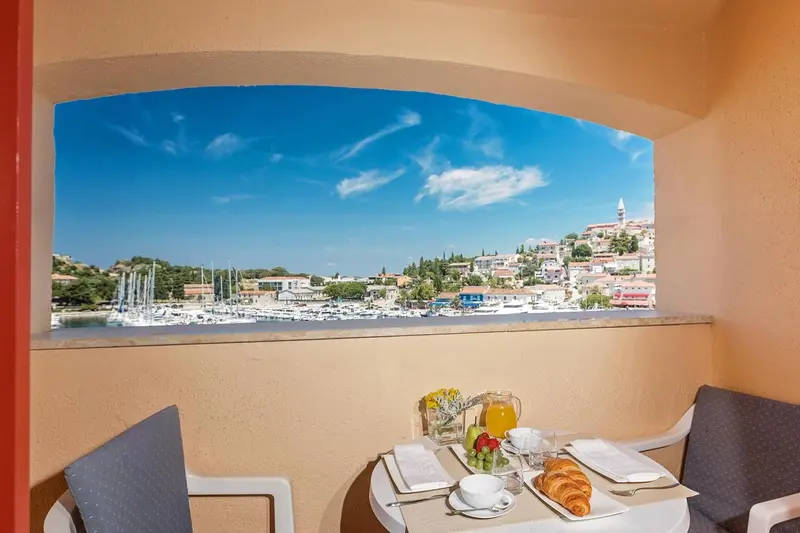 Une table est dressée devant une fenêtre ouverte sur un paysage côtier.