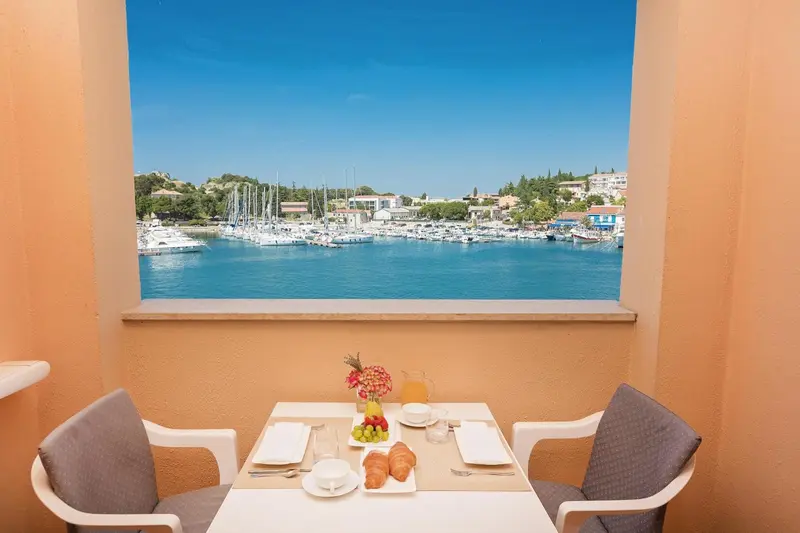 Une table est dressée sur un balcon avec vue sur un port de plaisance.