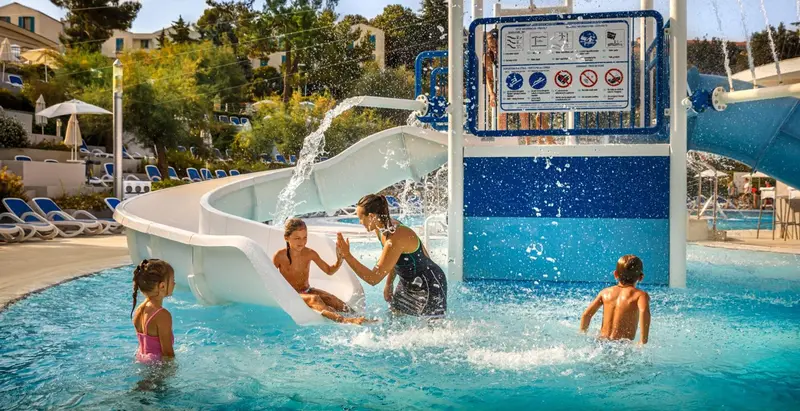 Enfants et adultes s'amusent dans une piscine avec un toboggan aquatique.