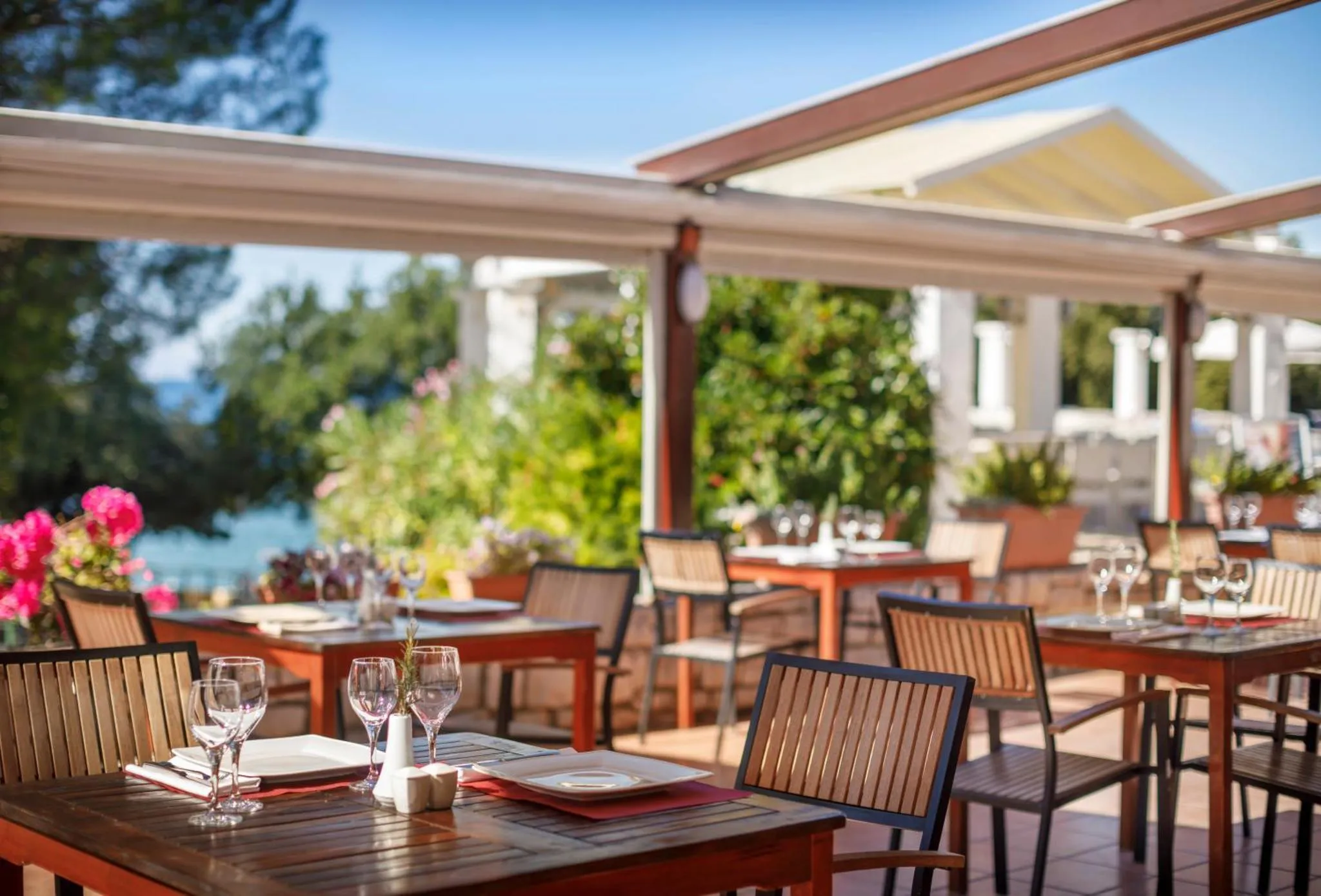 Tables dressées sur une terrasse ombragée avec vue sur la mer.