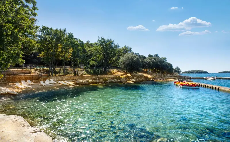 Des transats sont disposés sur une petite plage rocheuse au bord d'une eau turquoise.