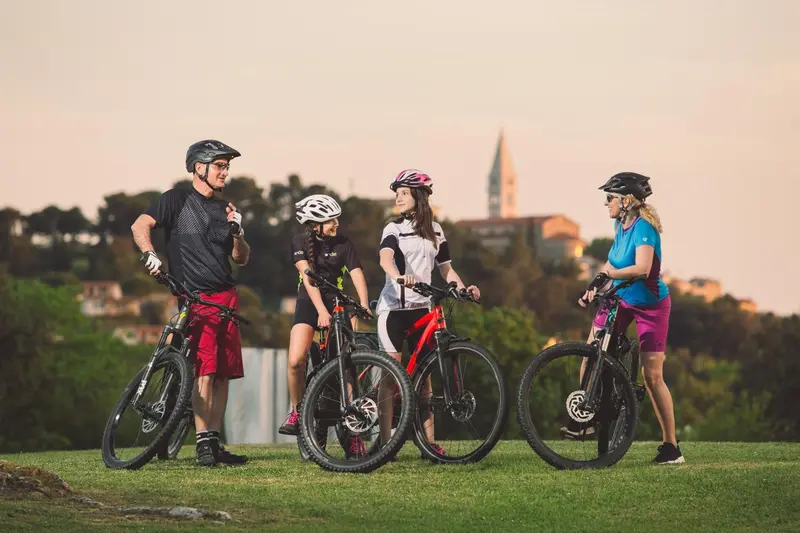 Une famille de cyclistes se tient sur une pelouse devant un paysage urbain.