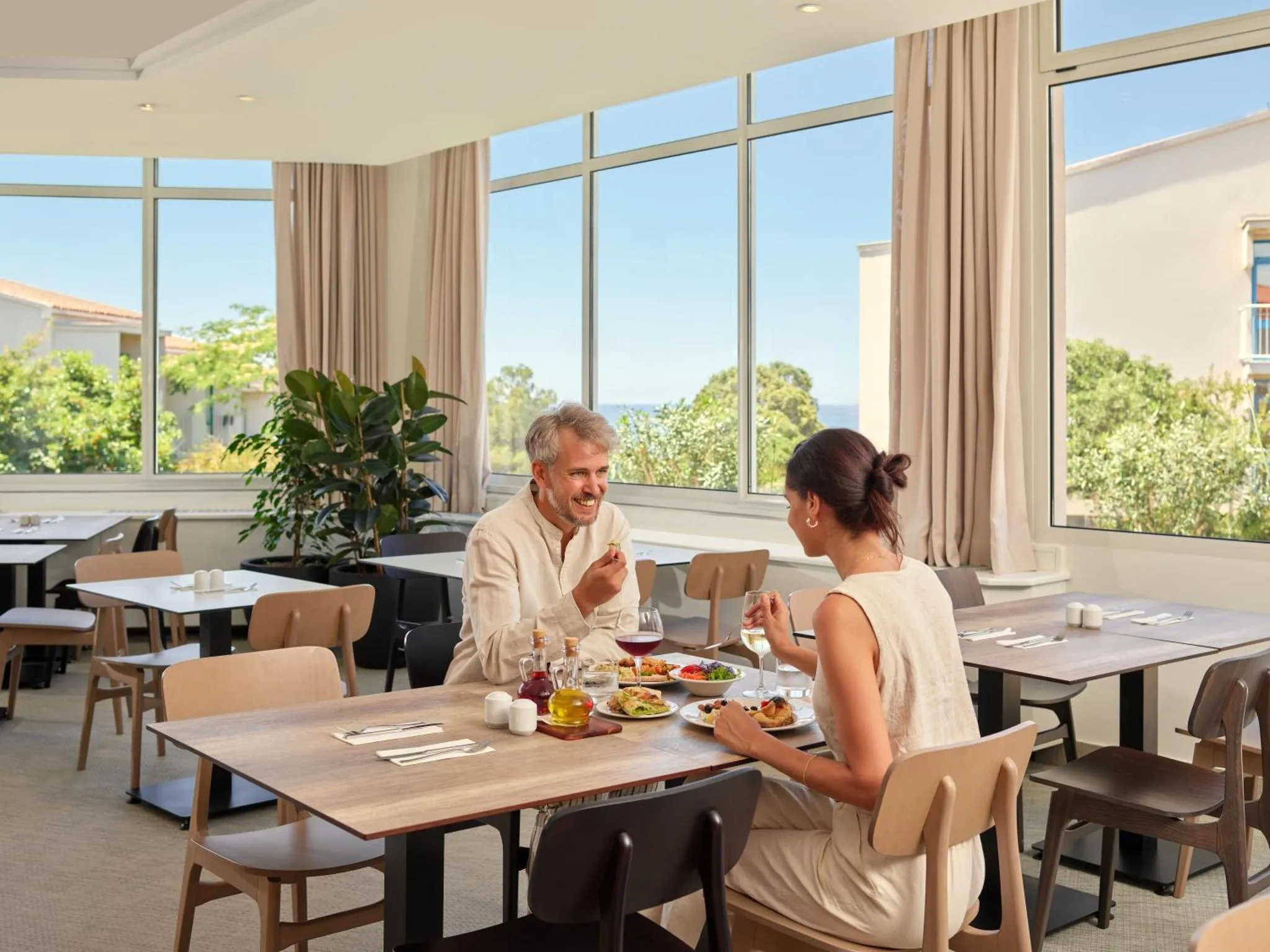 Un couple prend son repas à une table dans une salle lumineuse avec vue sur la mer.
