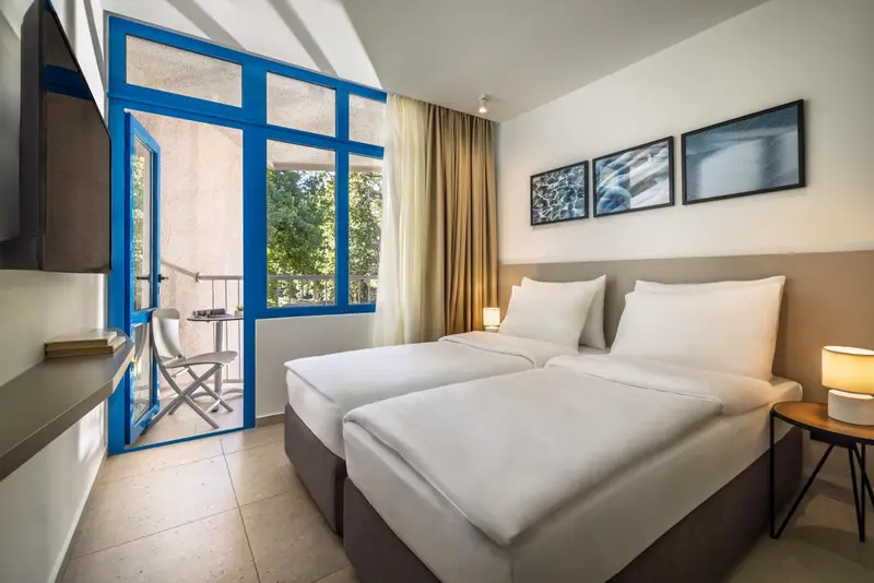 Une chambre lumineuse avec deux lits simples et un balcon.