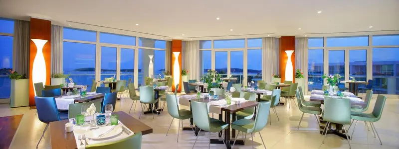 Une salle lumineuse avec des tables dressées face à une grande baie vitrée donnant sur la mer.