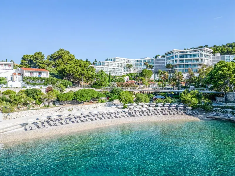Vue d'une plage de galets bordée de transats et d'un hôtel en hauteur.