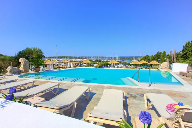 Transats blancs alignés au bord d'une piscine turquoise ensoleillée.