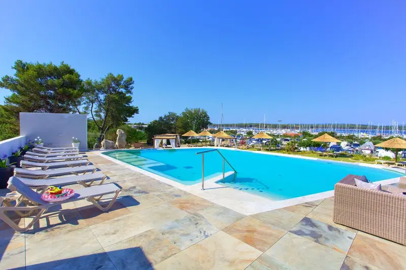 Transats et piscine au bord d'une marina ensoleillée.