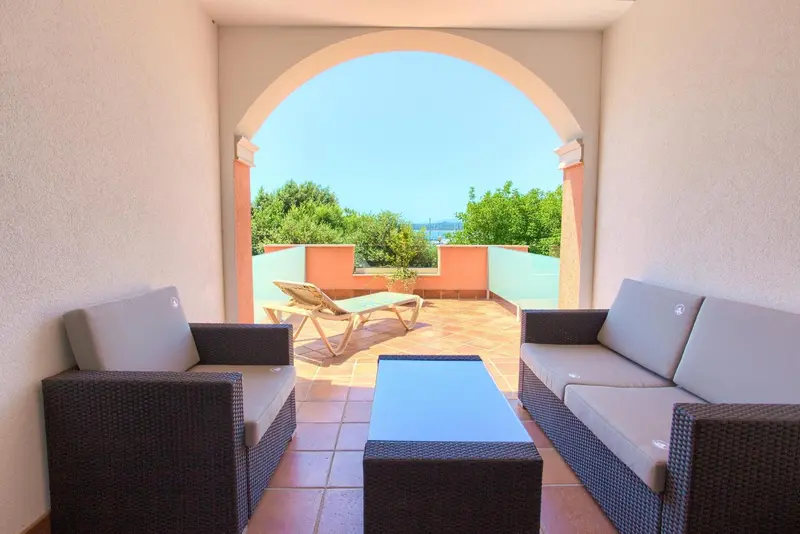 Terrasse aménagée avec canapés et chaises longues donnant sur un paysage verdoyant.