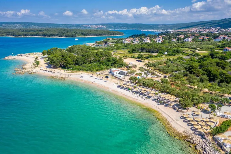 Vue aérienne d'une plage de sable fin bordée d'une eau turquoise et d'une végétation luxuriante.