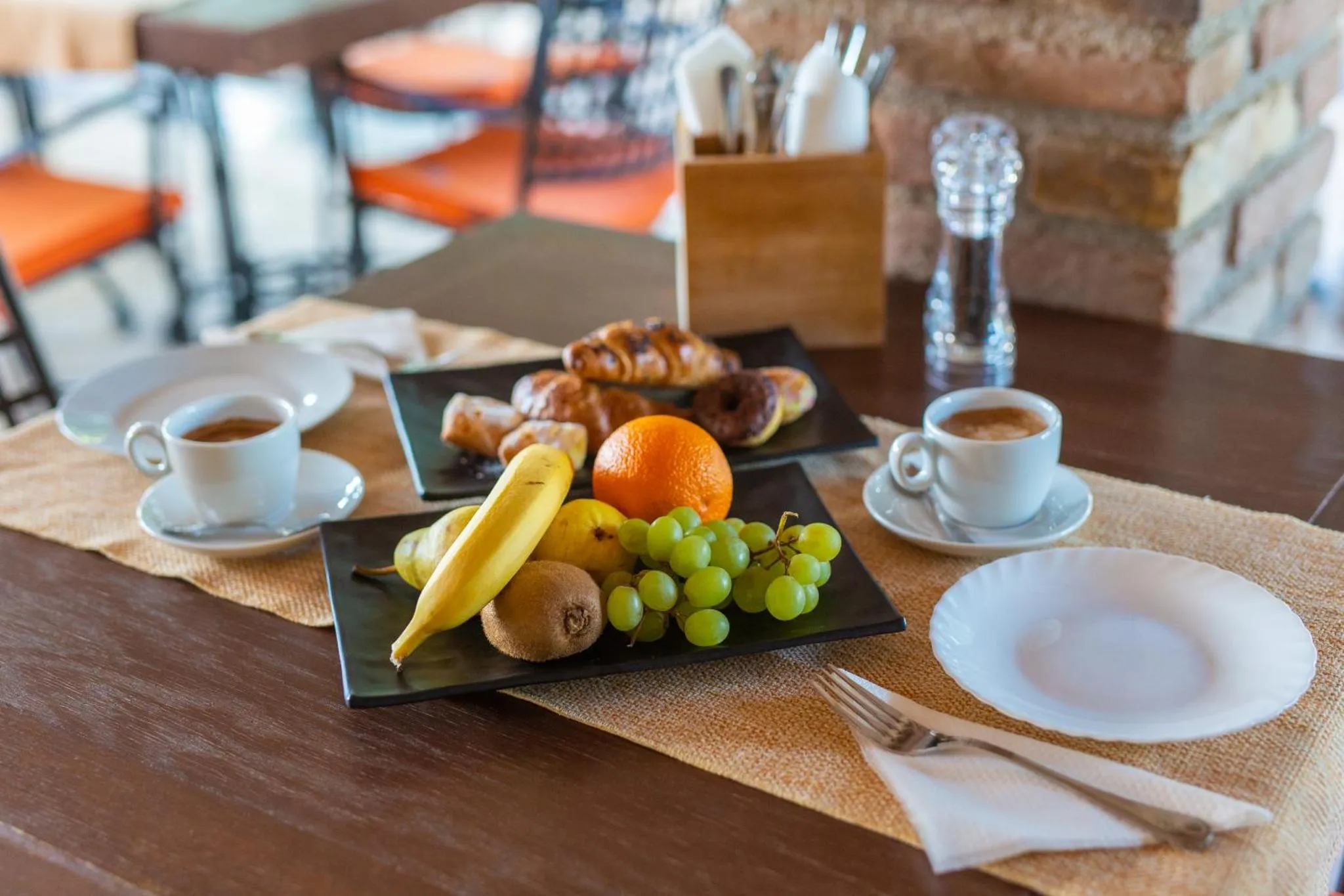Une table est dressée avec un petit-déjeuner composé de viennoiseries, de fruits et de boissons.