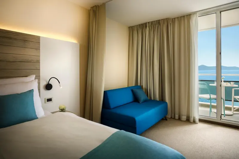 Chambre lumineuse avec un canapé bleu et un accès à un balcon.