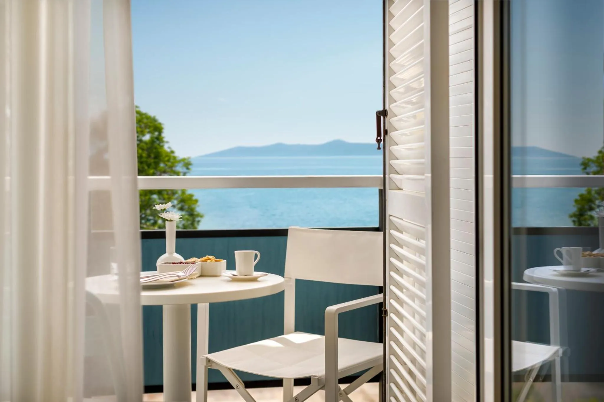 Une table ronde avec des couverts est posée sur un balcon avec vue sur la mer.