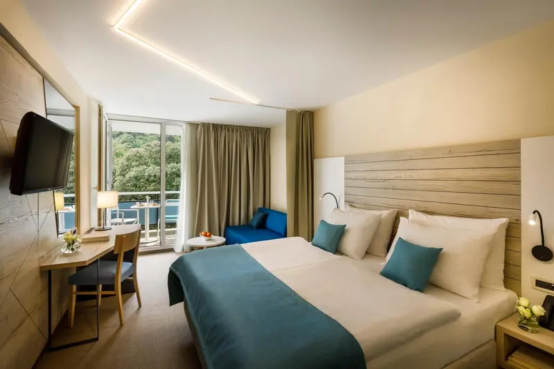 Chambre lumineuse avec un grand lit et un accès à un balcon.