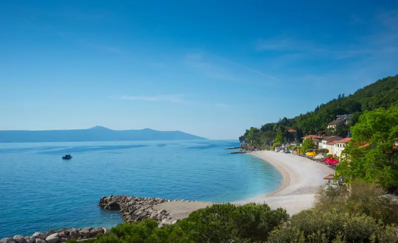 Une plage de galets bordée d'une eau turquoise et d'une végétation luxuriante.